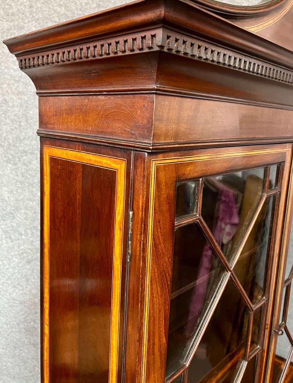 A Sheraton Revival mahogany cabinet featuring a swan-neck pediment, glazed upper doors with geometric bars, inlaid satinwood stringing, and multiple drawers set on tapered square legs. View IX
