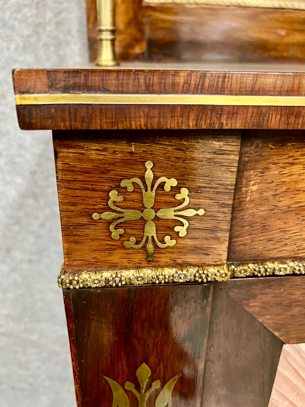 A Regency rosewood chiffonier featuring ornate brass marquetry inlay, twin doors with pleated fabric panels, and a raised top shelf supported by brass columns. View V