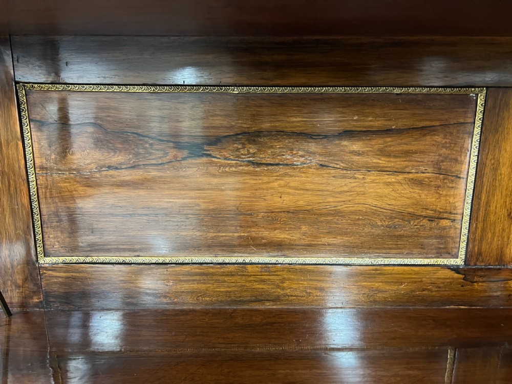A Regency rosewood chiffonier featuring ornate brass marquetry inlay, twin doors with pleated fabric panels, and a raised top shelf supported by brass columns. View IX