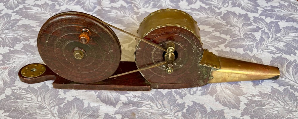 An antique mechanical rotary hearth bellows constructed from dark mahogany with a brass-trimmed cylinder housing, brass nozzle, and hand-crank pulley wheel.