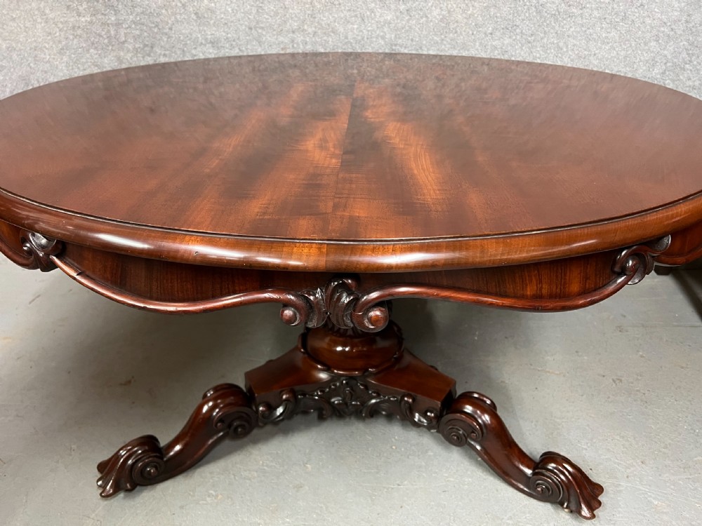 A circular Victorian mahogany tilt-top centre table displaying highly figured flame mahogany veneer on a carved tripod pedestal base. View II