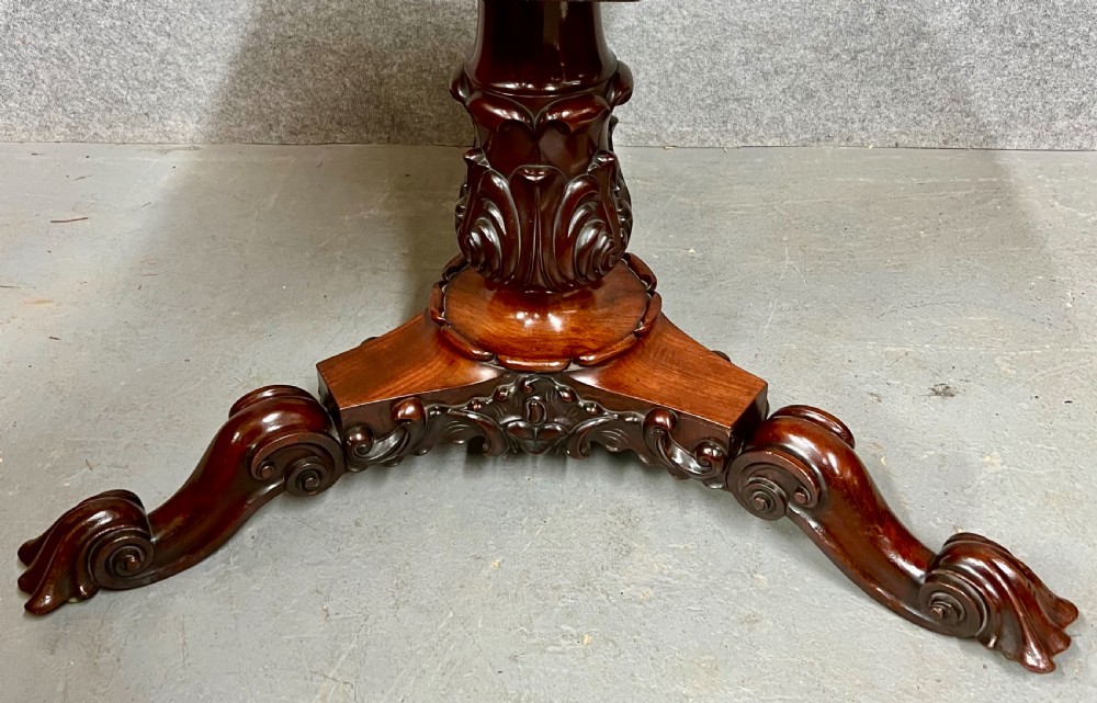 A circular Victorian mahogany tilt-top centre table displaying highly figured flame mahogany veneer on a carved tripod pedestal base. View VI
