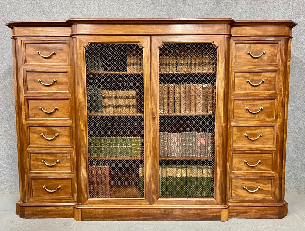 A large antique wooden breakfront library bookcase with twin central wire mesh doors flanked by stacks of six drawers on each side.