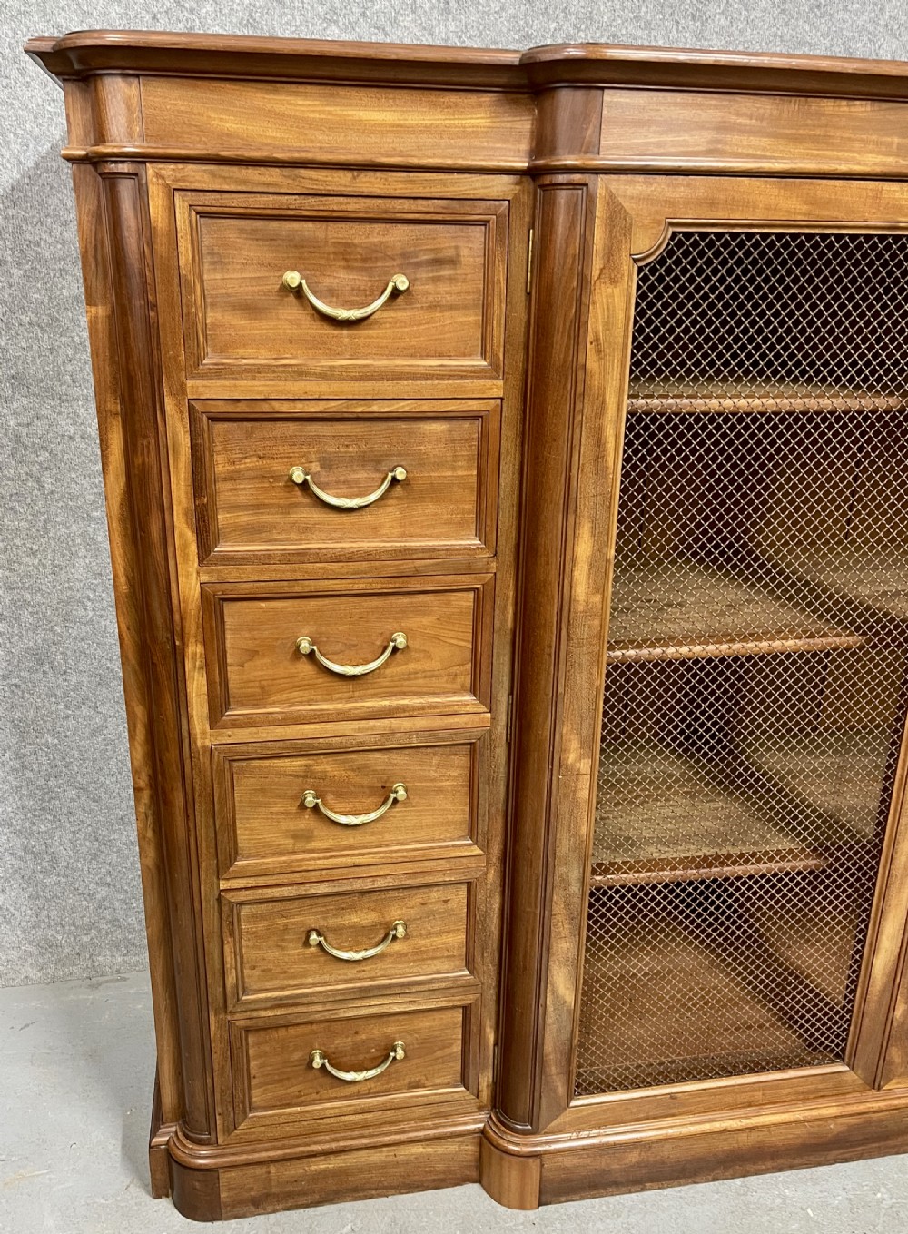 A large antique wooden breakfront library bookcase with twin central wire mesh doors flanked by stacks of six drawers on each side. View V