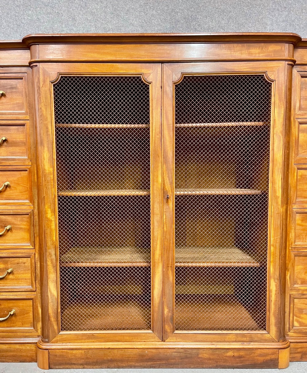 A large antique wooden breakfront library bookcase with twin central wire mesh doors flanked by stacks of six drawers on each side. View VI