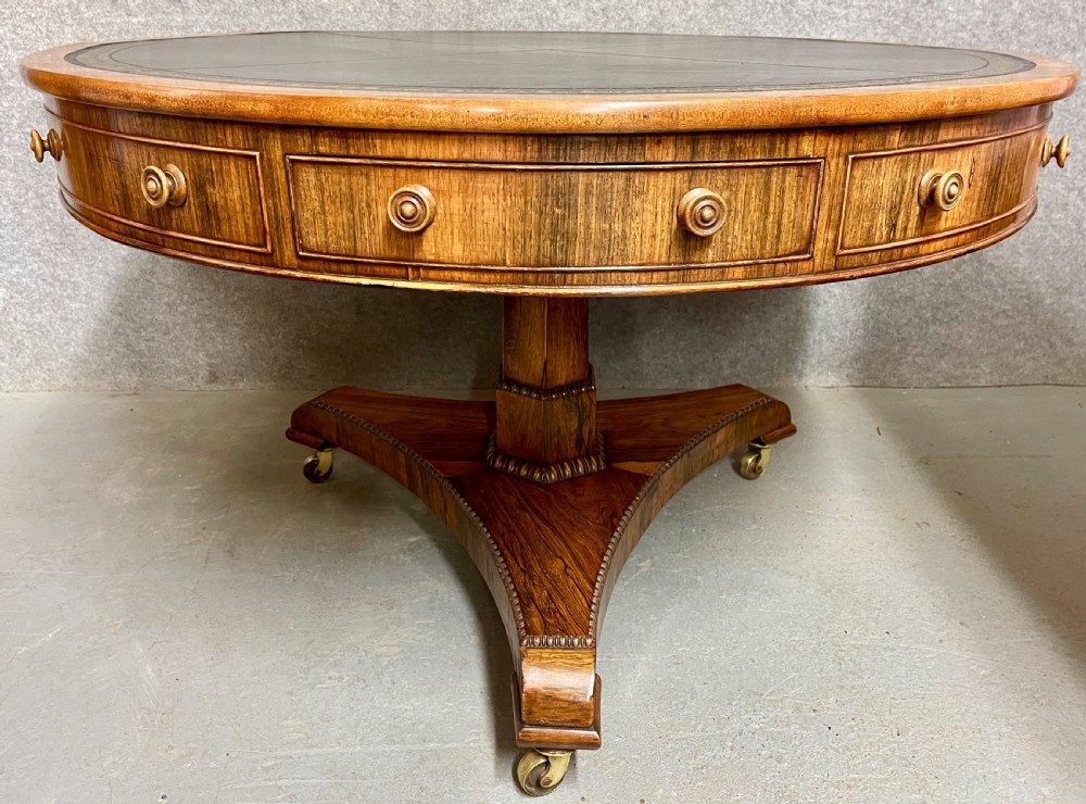A Regency period circular rosewood drum table featuring a black gold-tooled leather writing top, frieze drawers, and a tripartite pedestal base on brass castors. View III