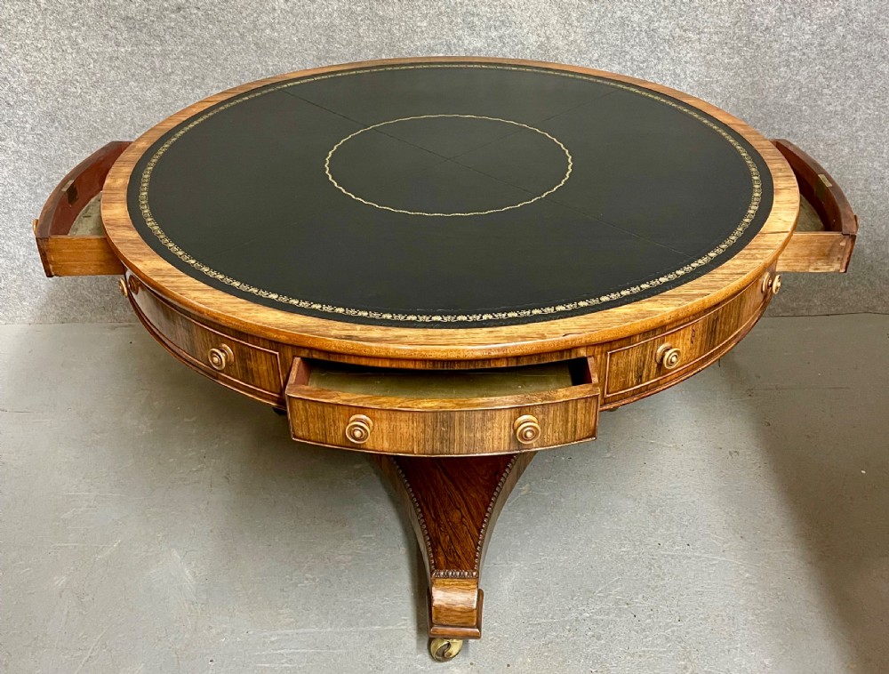 A Regency period circular rosewood drum table featuring a black gold-tooled leather writing top, frieze drawers, and a tripartite pedestal base on brass castors. View IV