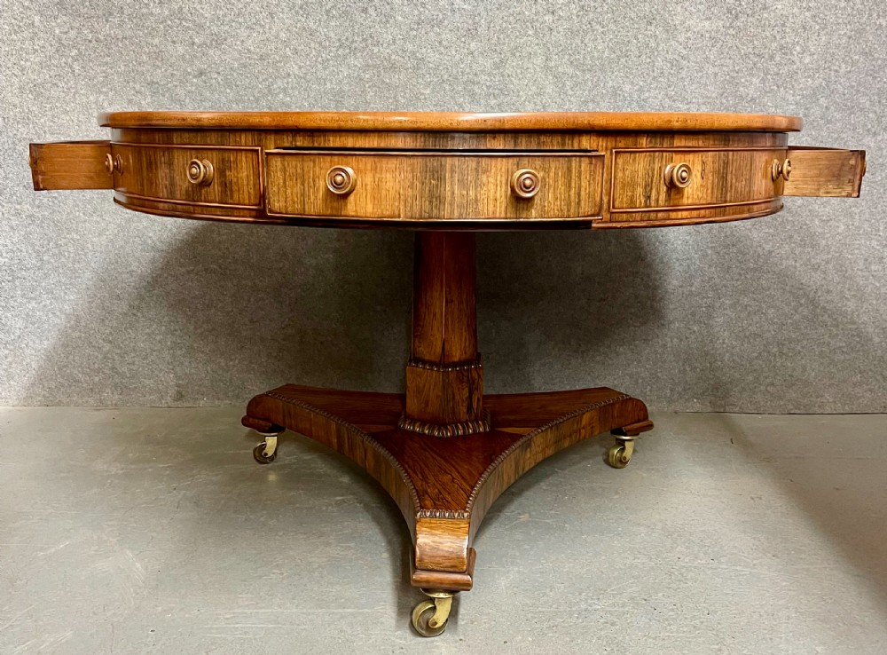 A Regency period circular rosewood drum table featuring a black gold-tooled leather writing top, frieze drawers, and a tripartite pedestal base on brass castors. View V