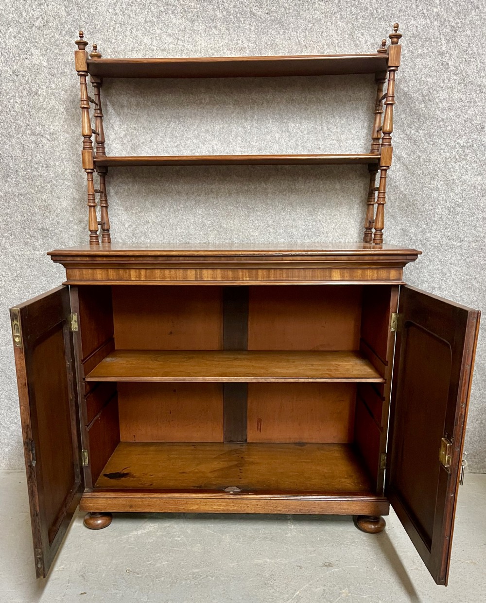 An antique mahogany chiffonier featuring two panelled cupboard doors with carved shell details below a tiered open bookcase supported by turned spindles. View II