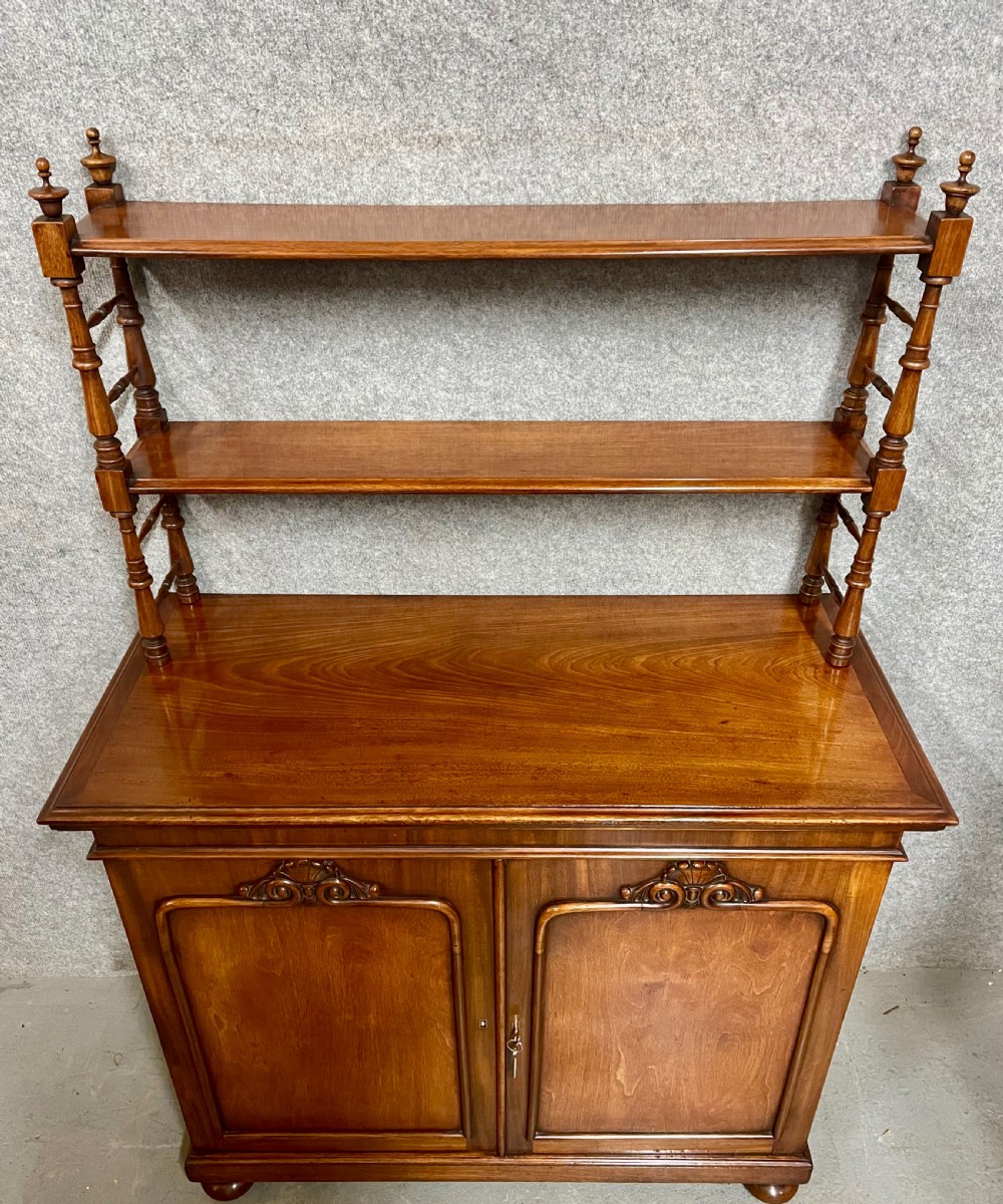 An antique mahogany chiffonier featuring two panelled cupboard doors with carved shell details below a tiered open bookcase supported by turned spindles. View V