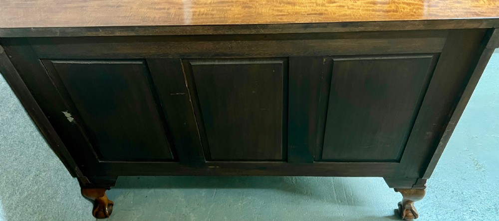 A semi-circular Chippendale style mahogany demi-lune side cabinet featuring flame mahogany veneers, a carved border, a central oval door panel, and carved claw and ball feet. View IX