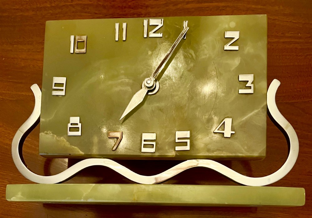 An Art Deco green onyx clock with stylized chrome numerals and hands supported on a serpentine chrome frame and stone base.