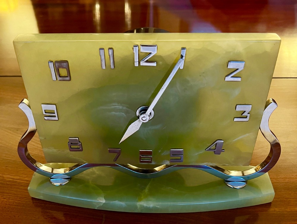 An Art Deco green onyx clock with stylized chrome numerals and hands supported on a serpentine chrome frame and stone base. View IV