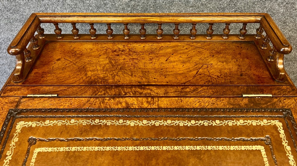 A Victorian walnut slide-top Davenport desk featuring a spindle gallery rail, leather writing surface, side drawers with turned knobs, and carved scroll supports. View II