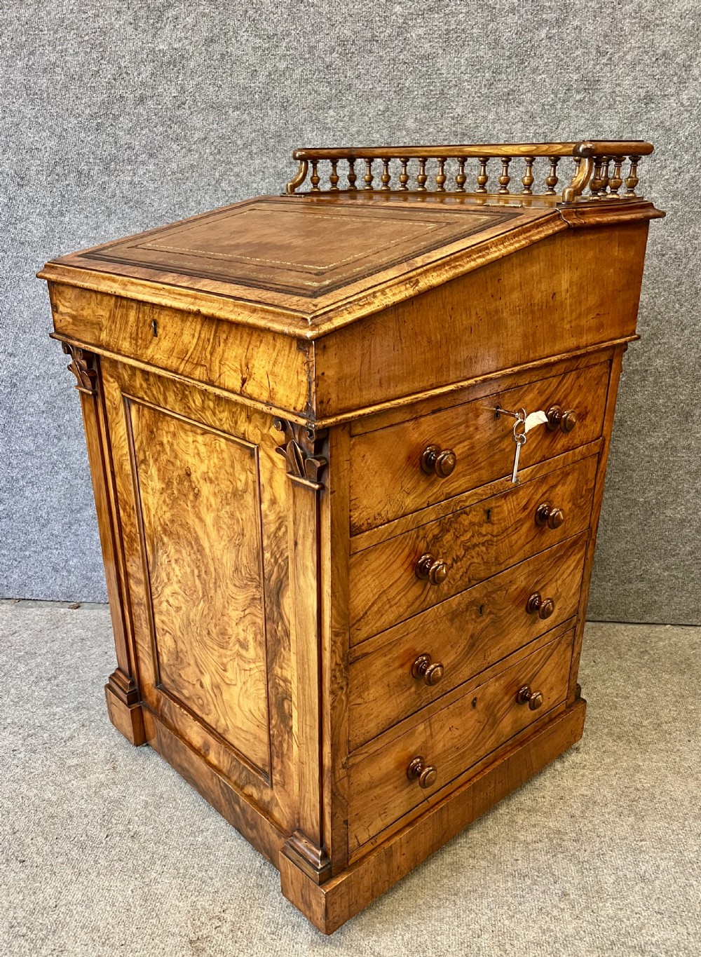 A Victorian walnut slide-top Davenport desk featuring a spindle gallery rail, leather writing surface, side drawers with turned knobs, and carved scroll supports.