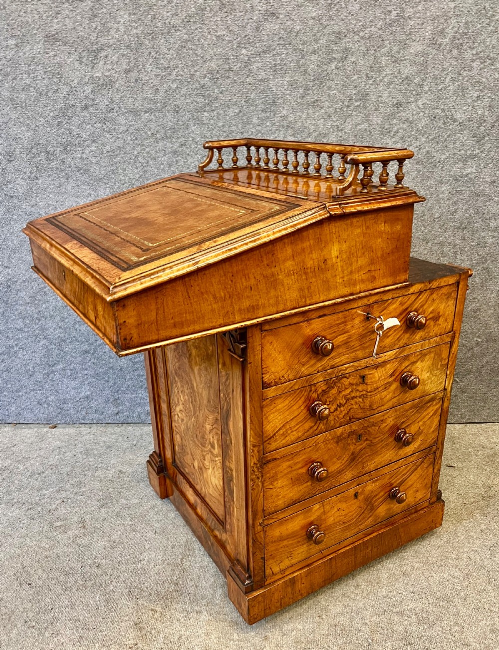 A Victorian walnut slide-top Davenport desk featuring a spindle gallery rail, leather writing surface, side drawers with turned knobs, and carved scroll supports. View III