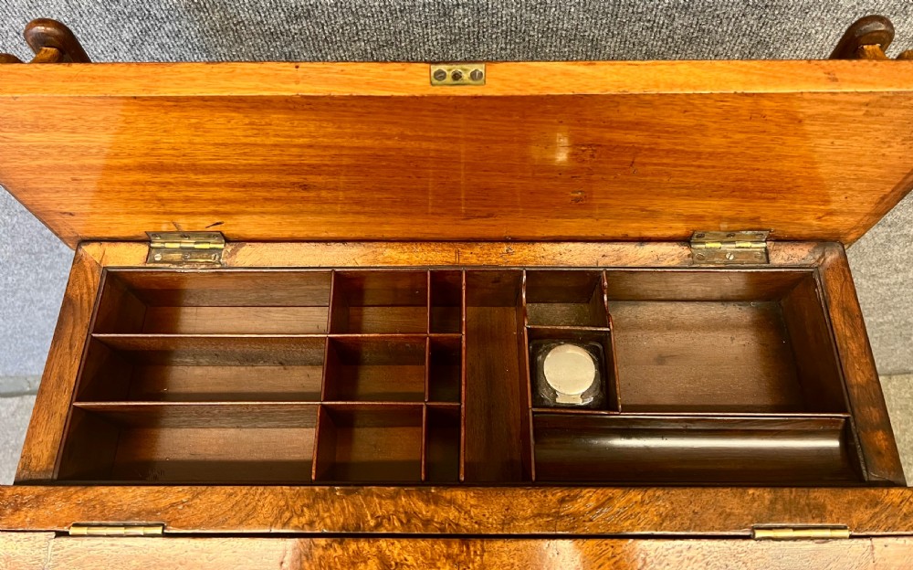 A Victorian walnut slide-top Davenport desk featuring a spindle gallery rail, leather writing surface, side drawers with turned knobs, and carved scroll supports. View IV