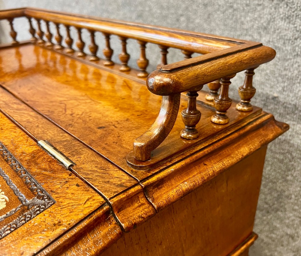 A Victorian walnut slide-top Davenport desk featuring a spindle gallery rail, leather writing surface, side drawers with turned knobs, and carved scroll supports. View V