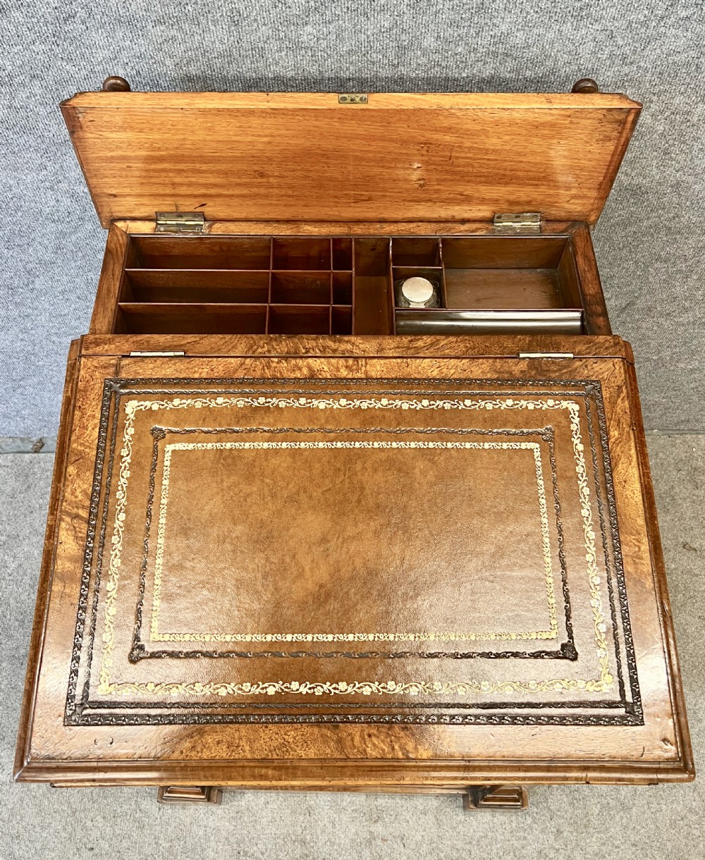 A Victorian walnut slide-top Davenport desk featuring a spindle gallery rail, leather writing surface, side drawers with turned knobs, and carved scroll supports. View VII