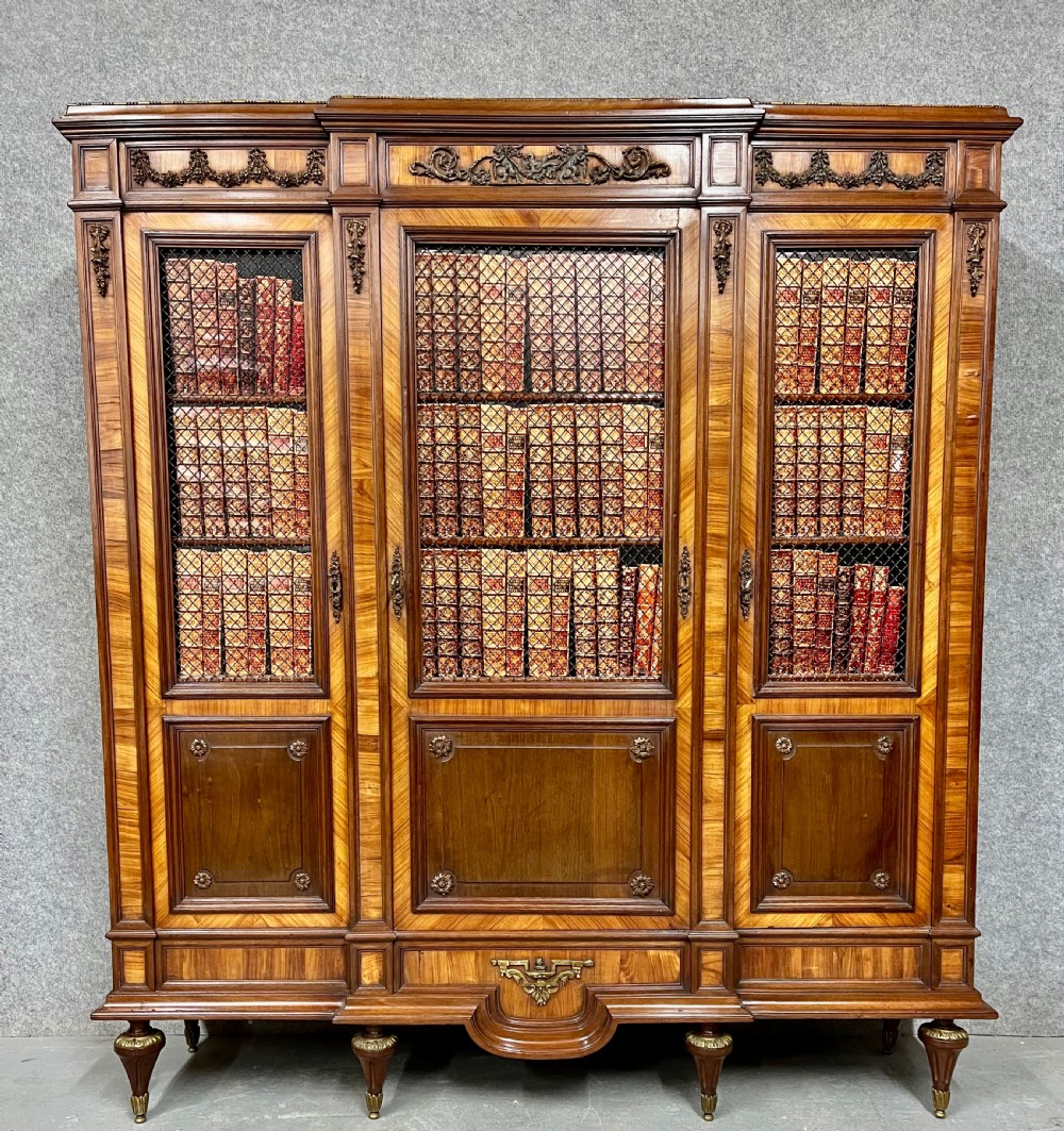 An antique French three-door bookcase crafted from kingwood and mahogany, featuring wire-mesh upper doors, lower timber panel doors, turned legs, and carved decorative crests.