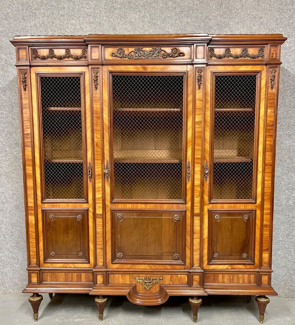 An antique French three-door bookcase crafted from kingwood and mahogany, featuring wire-mesh upper doors, lower timber panel doors, turned legs, and carved decorative crests. View II