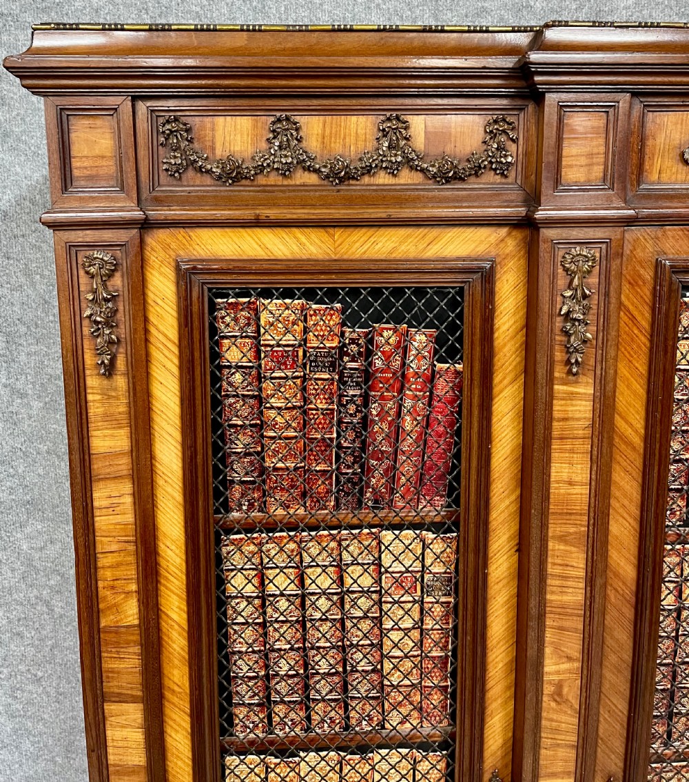 An antique French three-door bookcase crafted from kingwood and mahogany, featuring wire-mesh upper doors, lower timber panel doors, turned legs, and carved decorative crests. View V
