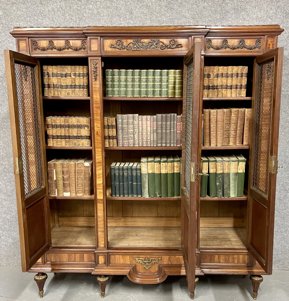 An antique French three-door bookcase crafted from kingwood and mahogany, featuring wire-mesh upper doors, lower timber panel doors, turned legs, and carved decorative crests. View VIII