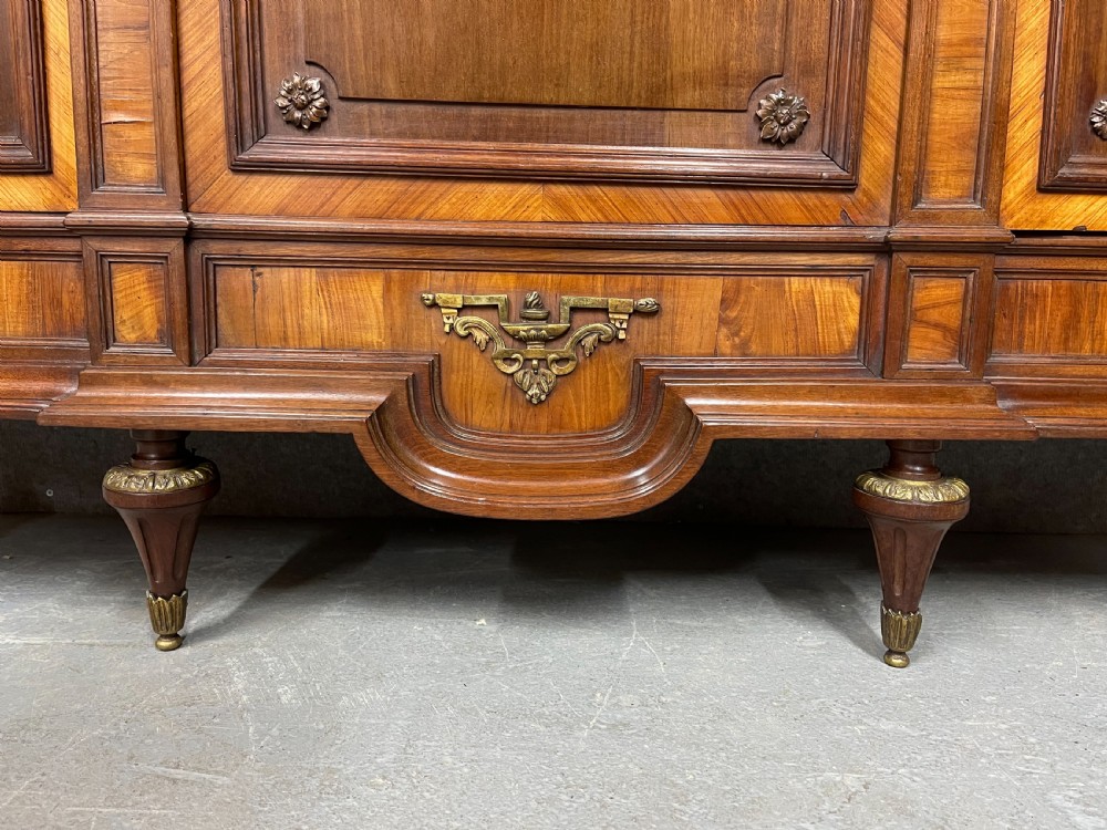 An antique French three-door bookcase crafted from kingwood and mahogany, featuring wire-mesh upper doors, lower timber panel doors, turned legs, and carved decorative crests. View XI