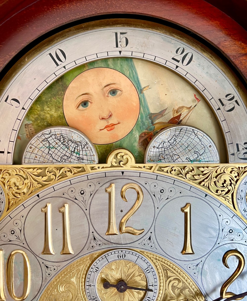 A tall Victorian carved mahogany musical longcase clock featuring spiral columns, a brass arch dial, visible brass weights, and tubular chimes behind a glass door. View IV
