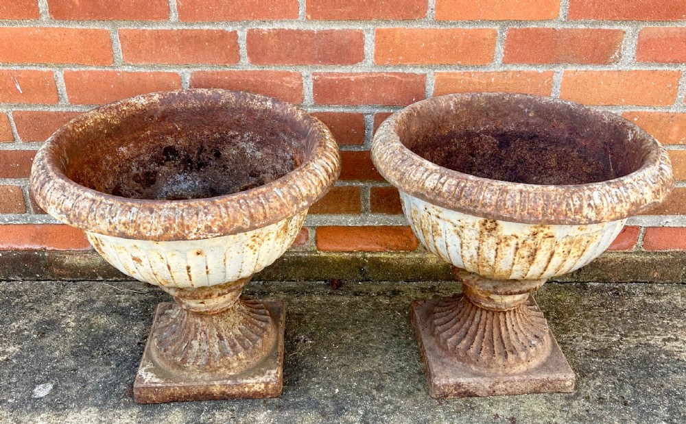 A pair of nineteenth-century fluted cast iron garden urns with weathered off-white paint and visible rust patina on square bases. View III