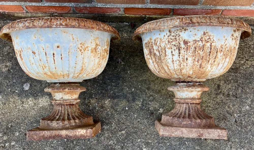 A pair of nineteenth-century fluted cast iron garden urns with weathered off-white paint and visible rust patina on square bases. View II
