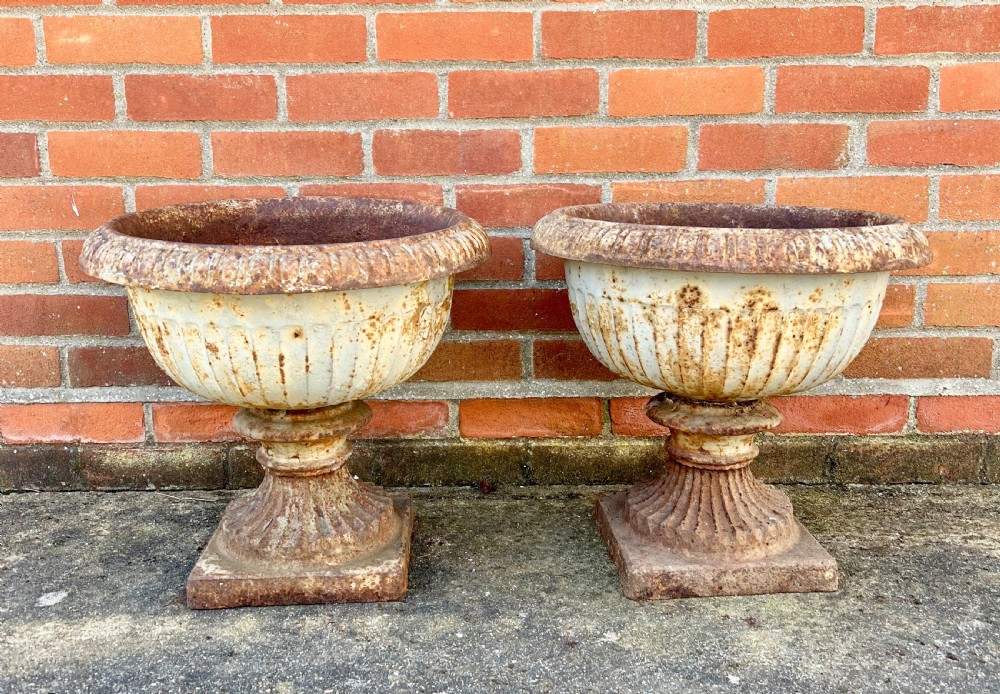 A pair of nineteenth-century fluted cast iron garden urns with weathered off-white paint and visible rust patina on square bases.