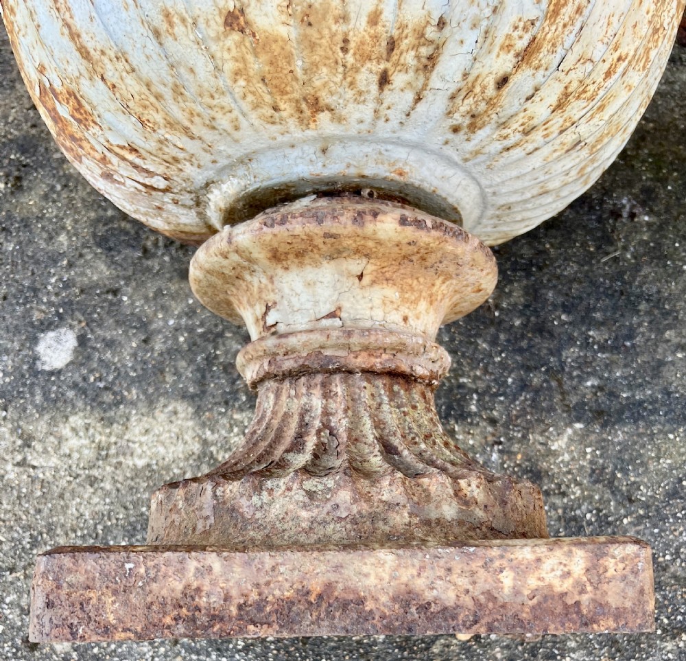A pair of nineteenth-century fluted cast iron garden urns with weathered off-white paint and visible rust patina on square bases. View IV