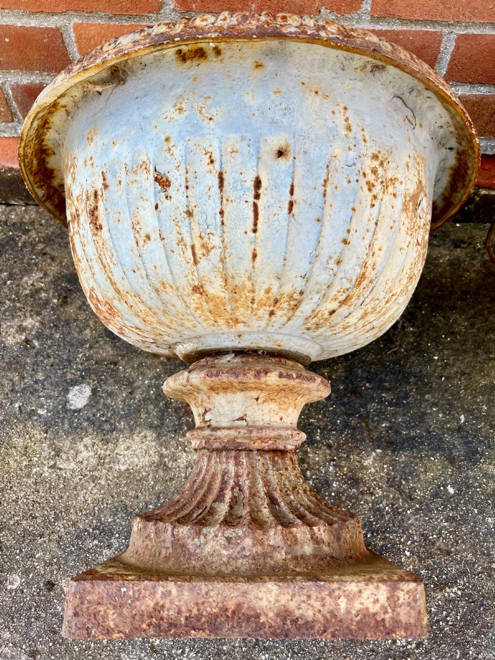 A pair of nineteenth-century fluted cast iron garden urns with weathered off-white paint and visible rust patina on square bases. View VI