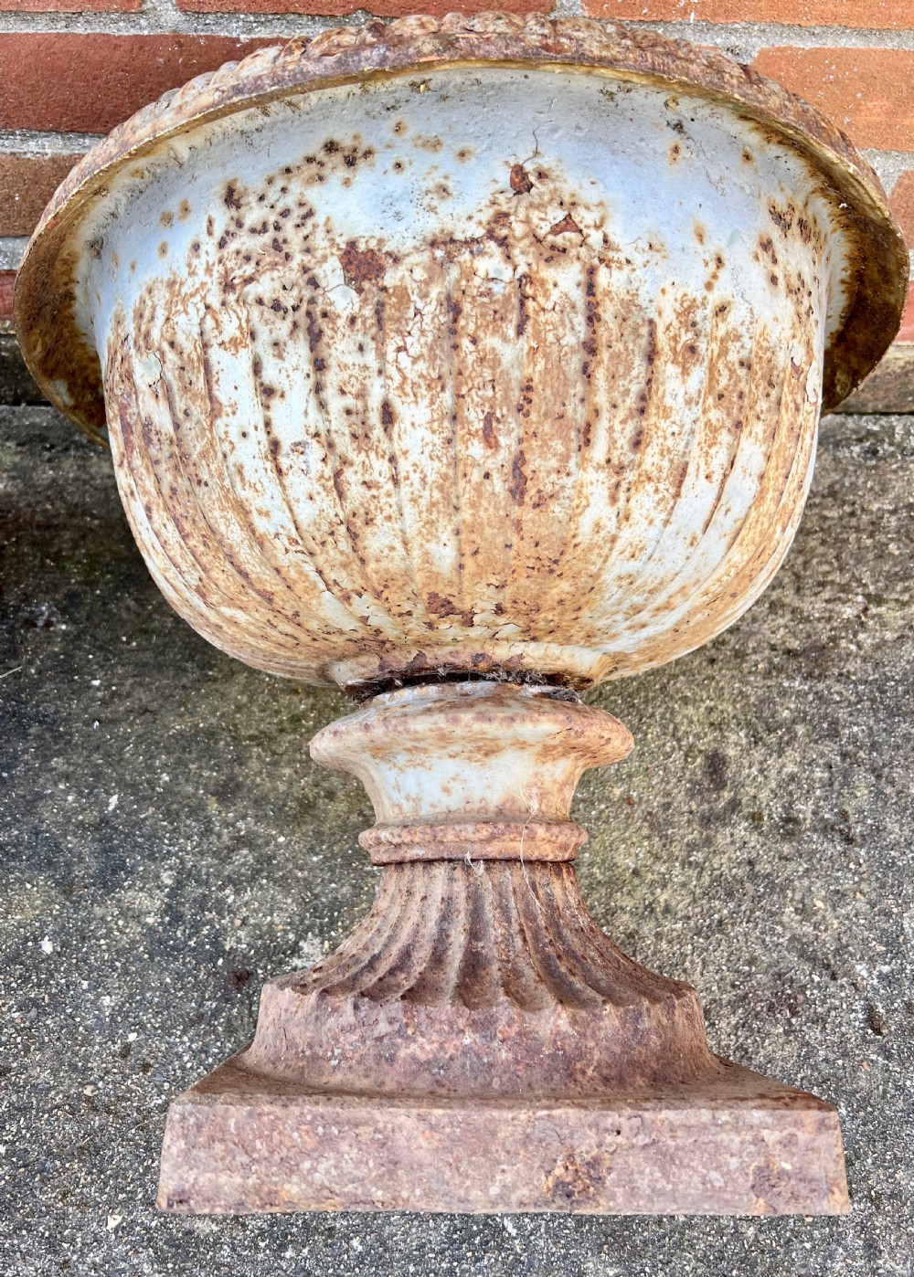 A pair of nineteenth-century fluted cast iron garden urns with weathered off-white paint and visible rust patina on square bases. View VII
