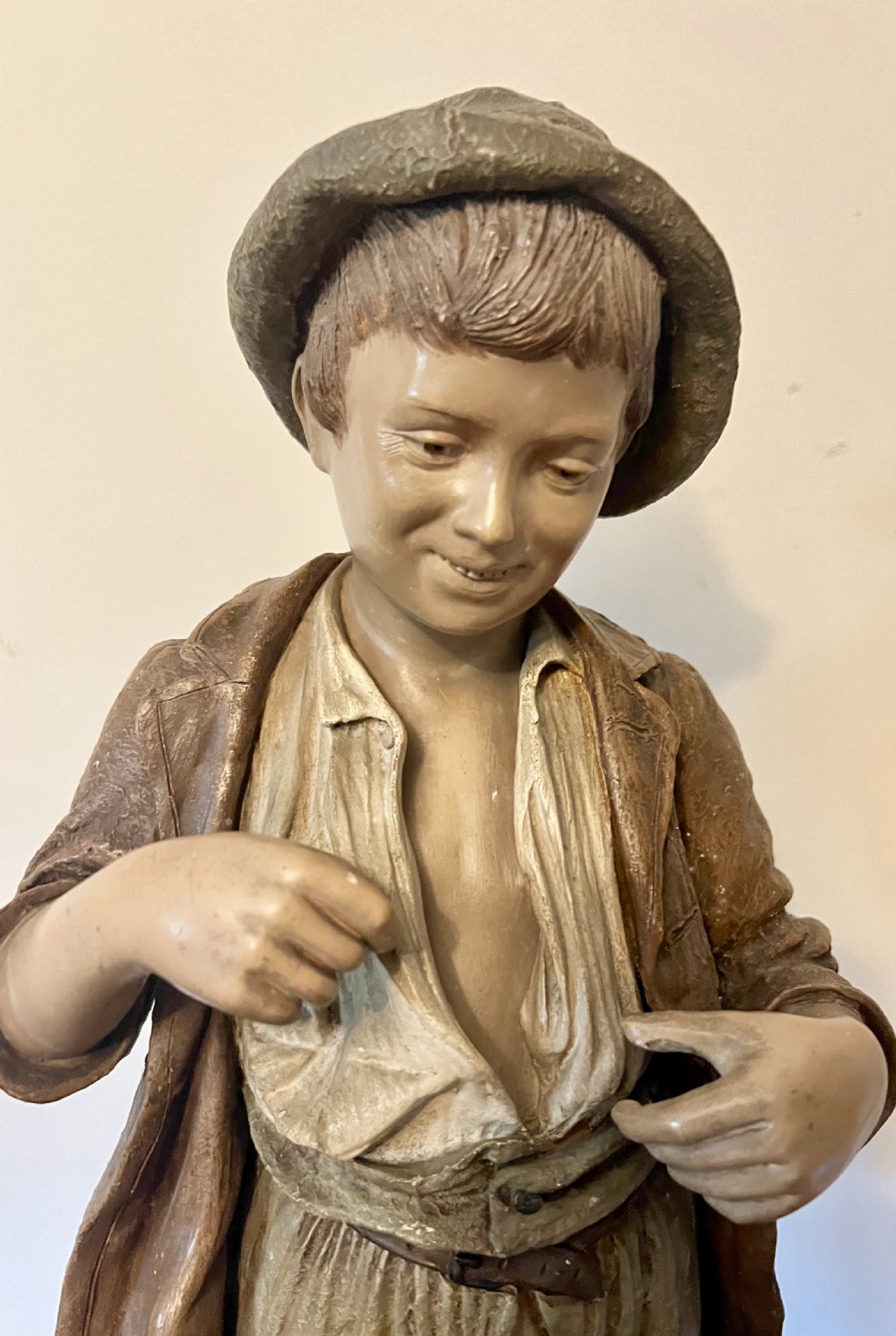 A polychrome terracotta sculpture depicting a young rustic boy in patched trousers and a wide-brimmed hat standing barefoot on a textured base. View II