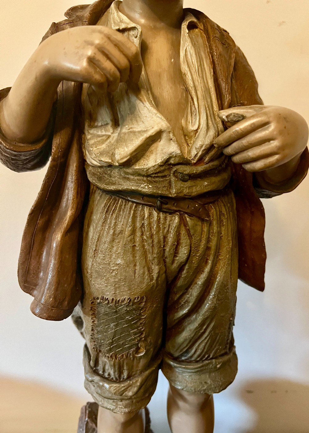 A polychrome terracotta sculpture depicting a young rustic boy in patched trousers and a wide-brimmed hat standing barefoot on a textured base. View V