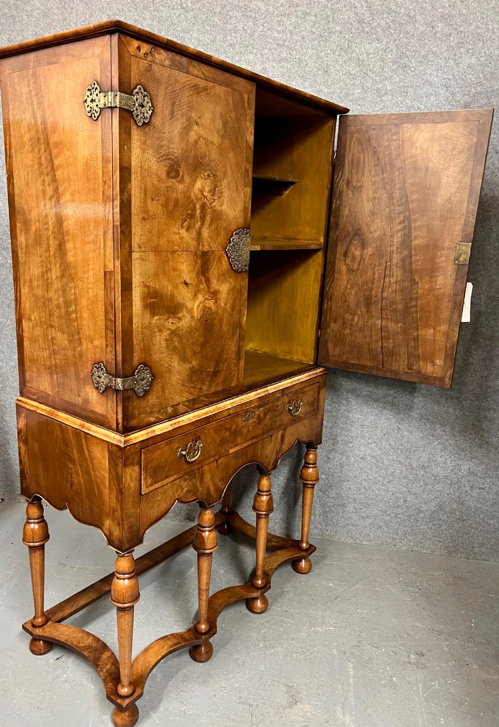 A William and Mary style burr walnut cocktail cabinet on stand featuring engraved brass strap hinges, double doors, a single drawer, turned legs, and a shaped stretcher. View III