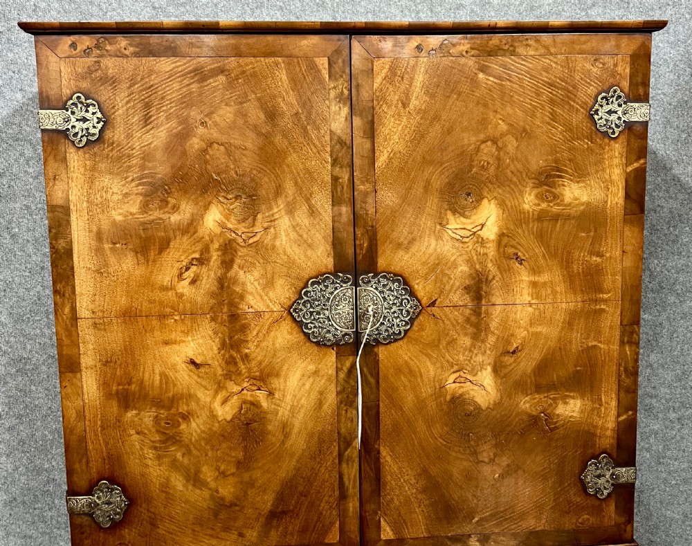 A William and Mary style burr walnut cocktail cabinet on stand featuring engraved brass strap hinges, double doors, a single drawer, turned legs, and a shaped stretcher. View XII