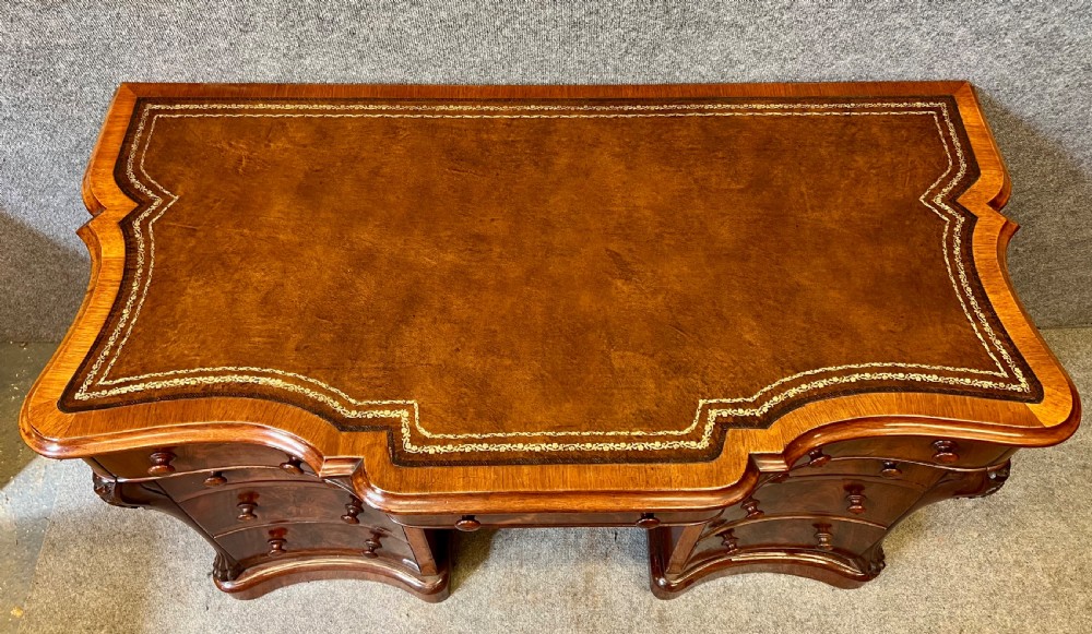 A Victorian figured mahogany pedestal desk featuring a shaped gilded leather surface, serpentine drawer fronts, and turned wooden knobs. View II