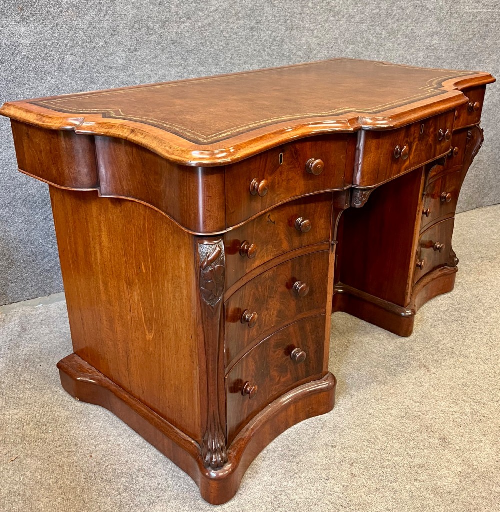 A Victorian figured mahogany pedestal desk featuring a shaped gilded leather surface, serpentine drawer fronts, and turned wooden knobs. View III