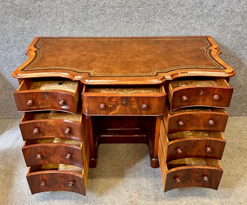 A Victorian figured mahogany pedestal desk featuring a shaped gilded leather surface, serpentine drawer fronts, and turned wooden knobs. View VI
