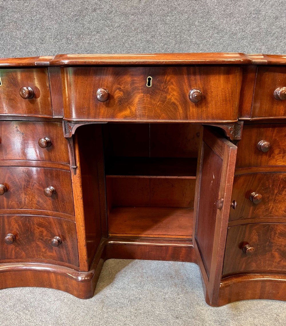 A Victorian figured mahogany pedestal desk featuring a shaped gilded leather surface, serpentine drawer fronts, and turned wooden knobs. View XI