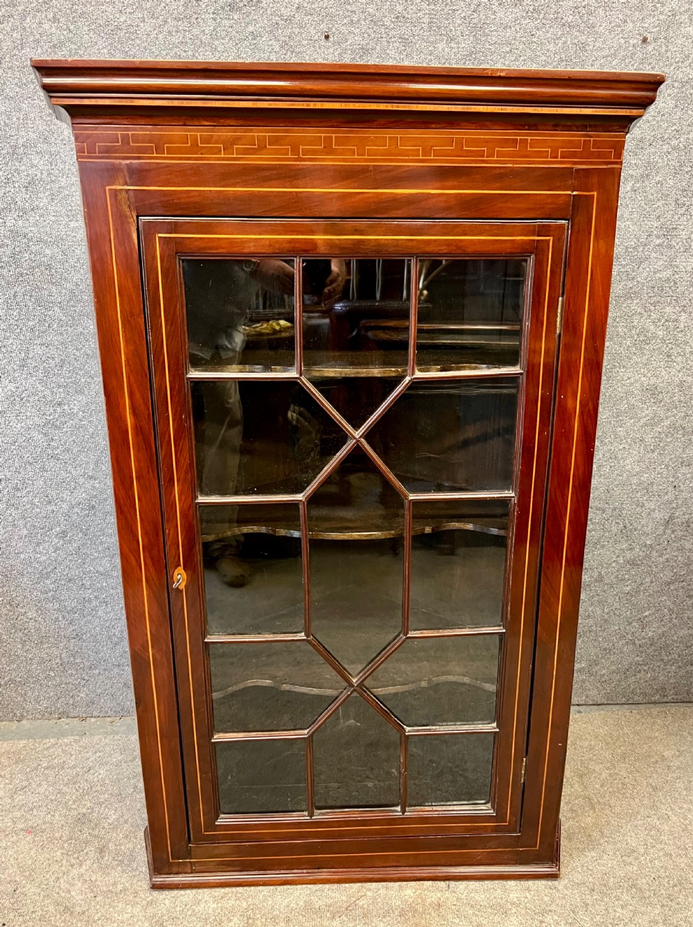 A George III hanging corner cupboard made of dark mahogany, featuring an astragal glazed door and decorative geometric inlay along the upper frieze.