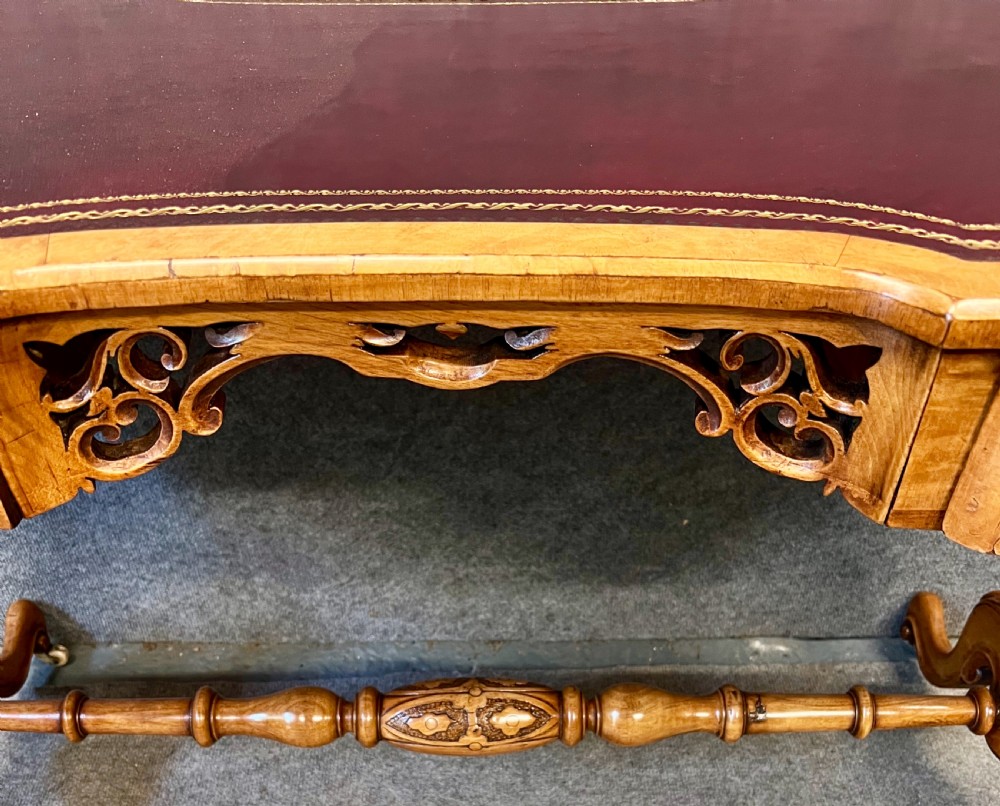 A Victorian burr walnut kidney-shaped writing desk featuring a burgundy leather writing surface, openwork carved frieze, turned central stretcher, and cabriole legs on brass castors. View VI