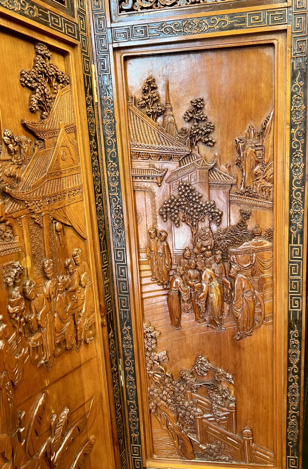 A six-panel wooden folding screen featuring high-relief carved scenes of figures, buildings, and plants framed by dark fretwork borders. View VIII