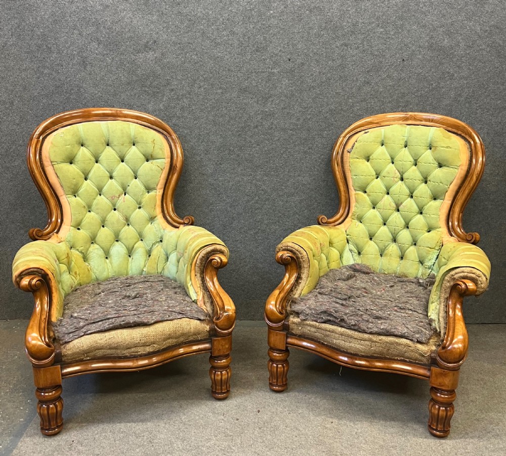 A pair of 1930s Victorian revival walnut armchairs featuring carved show-wood frames, button-back tufting, and worn green upholstery awaiting restoration.