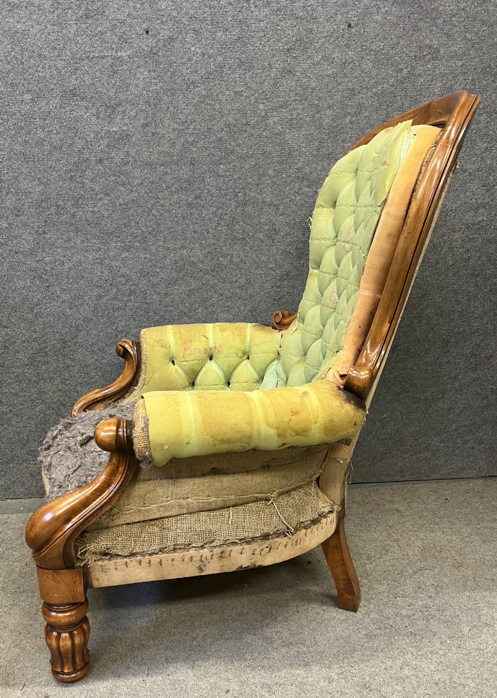 A pair of 1930s Victorian revival walnut armchairs featuring carved show-wood frames, button-back tufting, and worn green upholstery awaiting restoration. View V