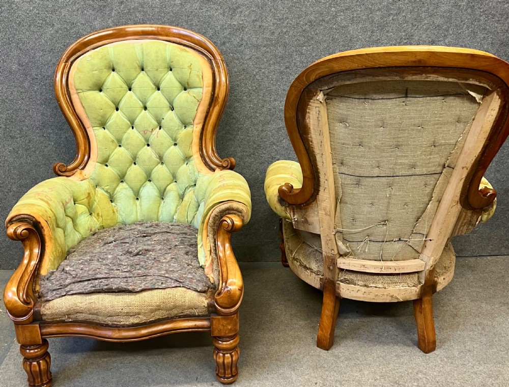 A pair of 1930s Victorian revival walnut armchairs featuring carved show-wood frames, button-back tufting, and worn green upholstery awaiting restoration. View VI