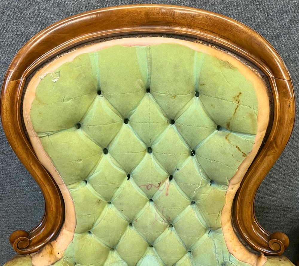 A pair of 1930s Victorian revival walnut armchairs featuring carved show-wood frames, button-back tufting, and worn green upholstery awaiting restoration. View VIII